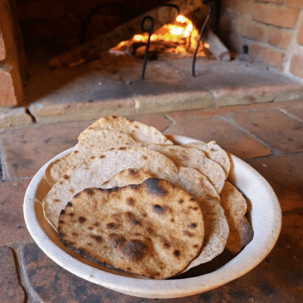 Bowl of freshly baked sourdough crispbread in front of a rustic wood-fired oven.