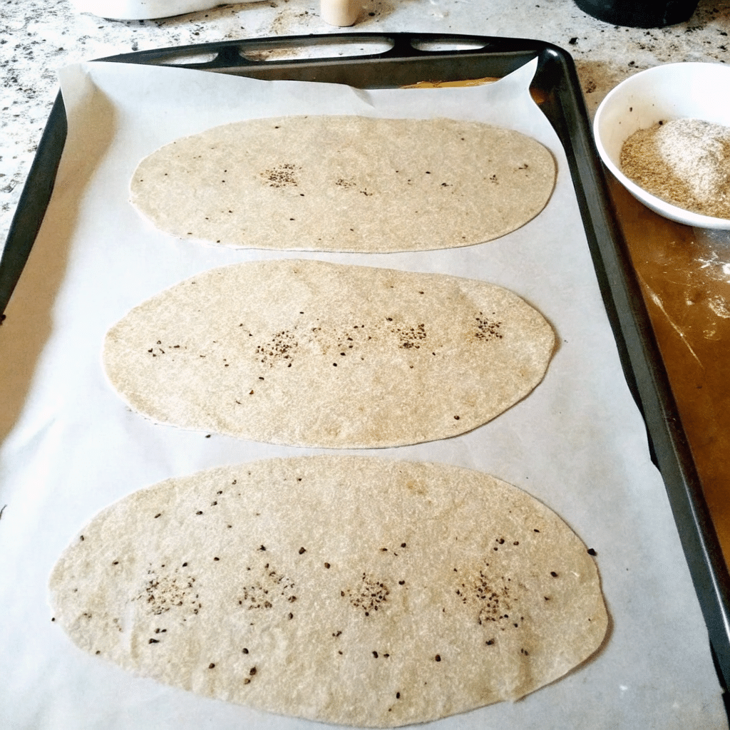 Rolled sourdough crispbread dough ovals with seeds on baking tray.