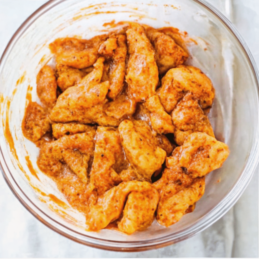 Butter chicken recipe showing marinated chicken pieces in a spiced, creamy sauce in a glass bowl