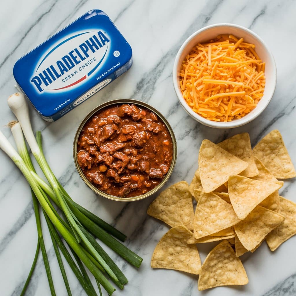 Ingredients for Philadelphia Cream Cheese Chili Dip including cream cheese, canned chili, shredded cheddar cheese, green onions, and tortilla chips.